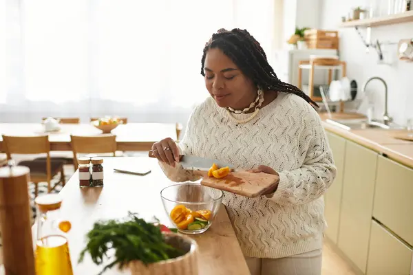 Uma jovem afro-americana habilmente chops ingredientes coloridos para uma salada refrescante em casa. — Fotografia de Stock