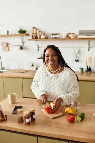 A young African American woman smiles while preparing a colorful salad in her bright kitchen. — Stock Photo