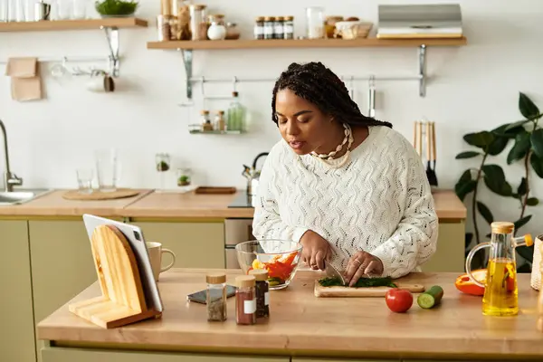 Uma jovem mulher negra chops legumes ao fazer uma salada fresca em sua cozinha ensolarada. — Fotografia de Stock