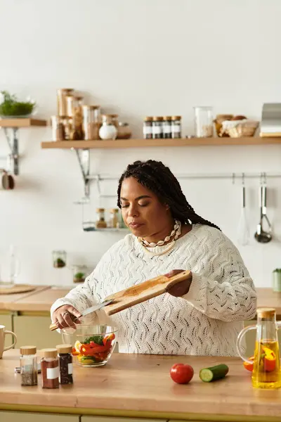 Uma jovem afro-americana prepara uma salada vibrante com legumes frescos em sua cozinha. — Fotografia de Stock