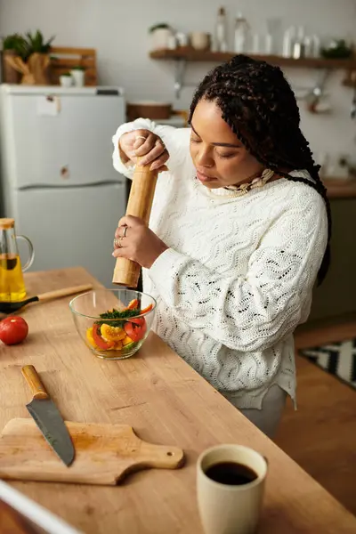 Young African American woman creates a colorful salad in her cozy kitchen, adding spices artfully. — Stock Photo