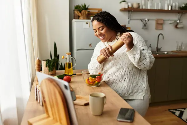 A young African American woman joyfully prepares a fresh salad in her cozy kitchen. — Stock Photo