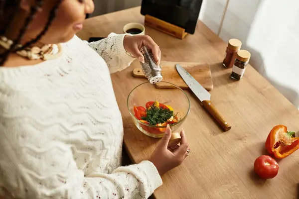 Uma jovem afro-americana mede cuidadosamente uma salada vibrante com amor em sua cozinha acolhedora.. — Fotografia de Stock