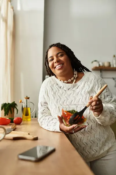 Uma jovem afro-americana feliz faz uma salada fresca em sua cozinha brilhante e acolhedora. — Fotografia de Stock