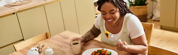Una giovane donna afroamericana assapora la sua insalata in una cucina accogliente piena di calore. — Foto stock