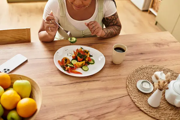 Uma jovem negra desfruta de uma salada fresca em sua mesa de cozinha, valorizando a alimentação saudável.. — Fotografia de Stock