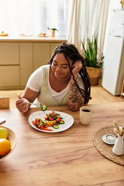 Uma jovem afro-americana saboreia uma deliciosa salada em sua cozinha acolhedora durante o almoço. — Fotografia de Stock