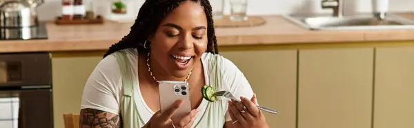 Uma jovem afro-americana delicia-se com uma salada fresca enquanto usa seu telefone em casa, banner — Fotografia de Stock