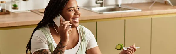 Uma jovem feliz senta-se confortavelmente em casa, desfrutando de uma salada fresca enquanto fala ao telefone. — Fotografia de Stock
