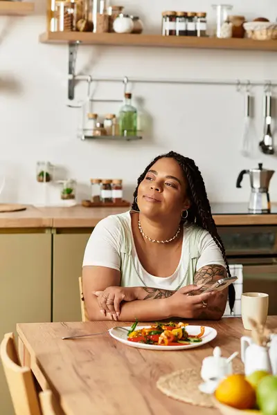 Em uma cozinha caseira brilhante, uma jovem afro-americana saboreia uma salada fresca durante o almoço. — Fotografia de Stock