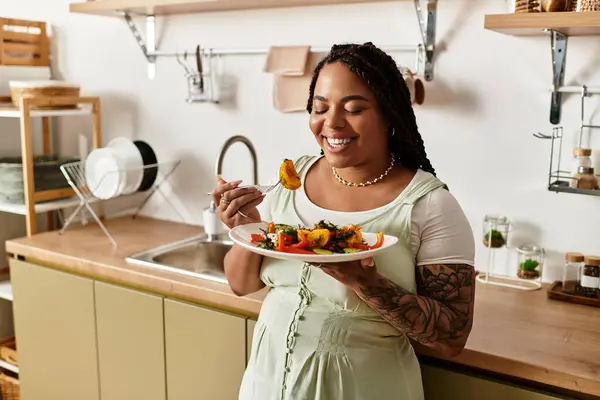 Eine junge afrikanisch-amerikanische Frau genießt zu Hause fröhlich einen bunten Salat zum Mittagessen. — Stockfoto