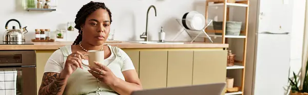 A young African American woman sips coffee as she works on her laptop in a bright kitchen space, banner — Stock Photo