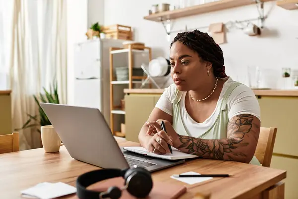 Jeune femme afro-américaine s'engage dans un travail à distance dans sa cuisine confortable, axée sur ses tâches. — Photo de stock