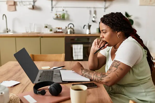 Giovane donna si siede a un tavolo di legno, concentrandosi sul suo computer portatile mentre si lavora da casa. — Foto stock