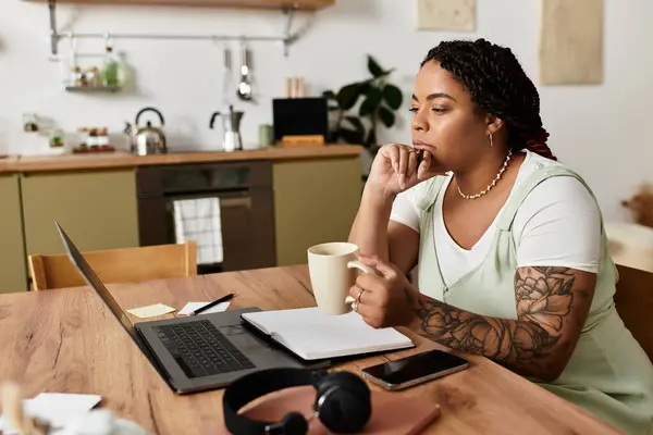 Mujer comprometida en el trabajo remoto estudia cuidadosamente su computadora portátil mientras toma té en casa. - foto de stock