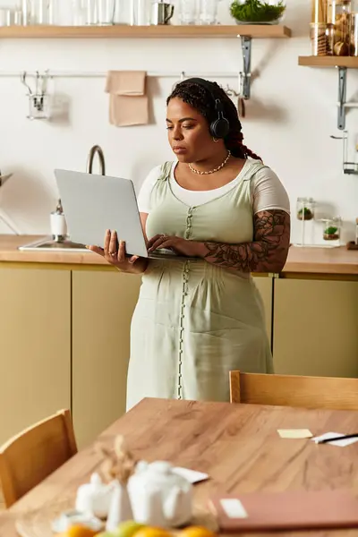 Focused young woman with headphones works on her laptop in a cozy home kitchen setting. — Stock Photo