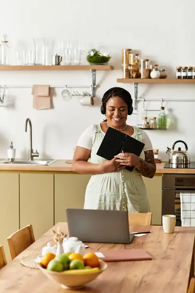 A young african american woman smiles while working on her laptop in a modern kitchen. — Stock Photo