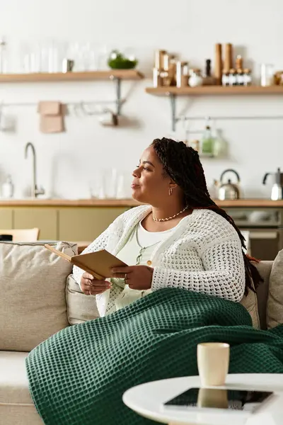 Young African American woman enjoys a peaceful morning at home with a book and warm drink. — Stock Photo