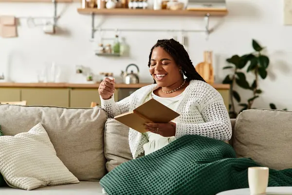 Junge Frau genießt einen friedlichen Morgen beim Lesen, während sie zu Hause in eine weiche Decke gehüllt ist. — Stockfoto