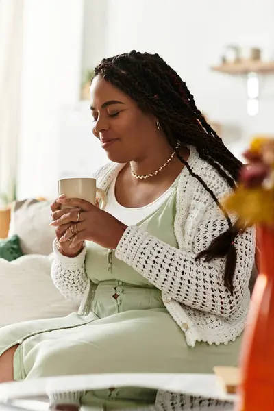 A young African American woman savoring a warm drink in her cozy living room space. — Stock Photo