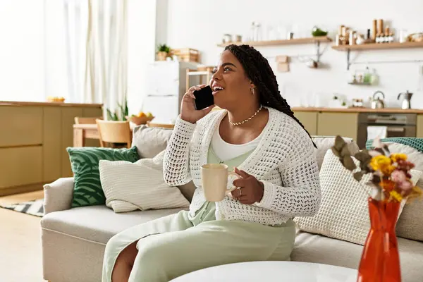 Uma jovem afro-americana relaxa em casa, tomando café e conversando ao telefone. — Fotografia de Stock