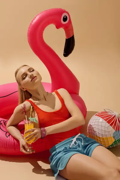 Young woman relaxes in summer attire while savoring a drink beside a bright flamingo float — Stock Photo