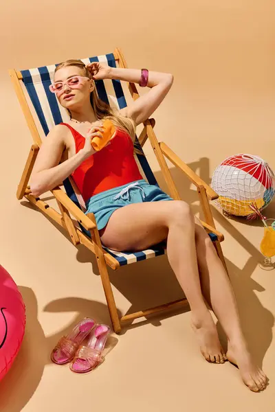 Young woman in a red swimsuit enjoys a tropical drink while lounging in a deck chair. — Stock Photo