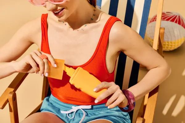 A vibrant young woman in stylish attire enjoys the sun, applying sunscreen during a beach outing. — Stock Photo