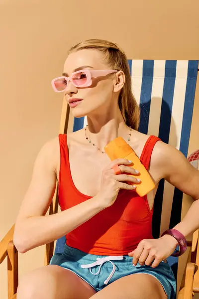 Eine Frau in trendiger Badebekleidung genießt ein buntes Eis am Stiel auf einem Liegestuhl in der Sonne. — Stockfoto