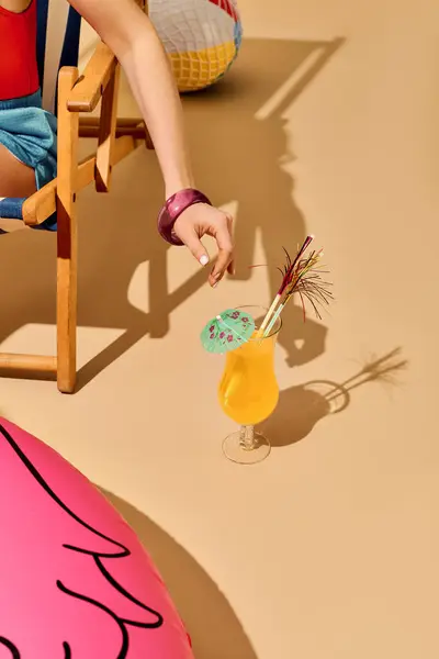 A young beautiful woman playfully reaches for her vibrant drink while relaxing on a sunny day. — Stock Photo