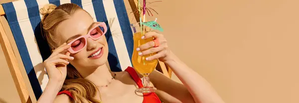 Una joven hermosa mujer descansa en una silla, saboreando una bebida tropical mientras toma el sol. - foto de stock