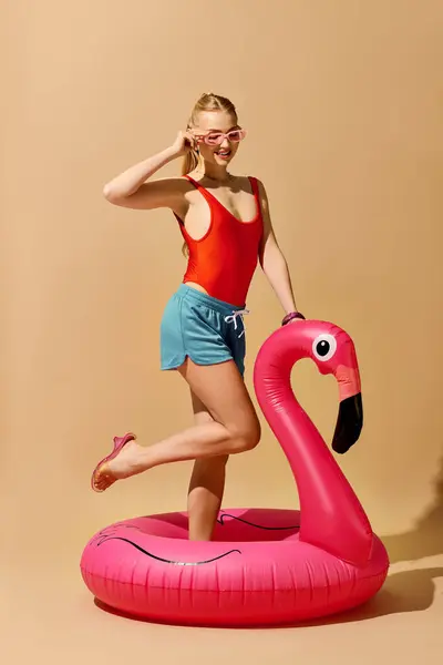 Junge Frau posiert auf einem rosafarbenen Flamingo-Wagen und zeigt ihr stylisches Sommer-Outfit. — Stockfoto