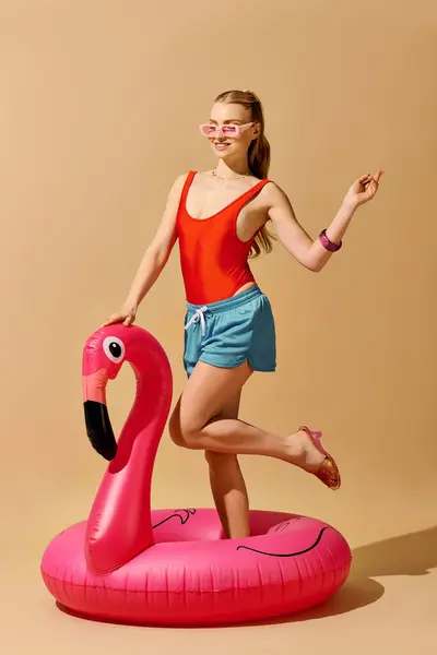 Helle und fröhliche junge Frau genießt verspielte Sommerstimmung, während sie auf einem rosafarbenen Flamingo-Wagen posiert. — Stockfoto