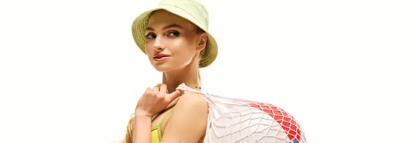 Mujer joven de moda muestra una bolsa de red llena de elementos vibrantes, abrazando vibraciones de verano. - foto de stock