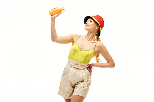 A stylish young woman in a vibrant outfit playfully holds a drink, radiating joy and confidence. — Stock Photo