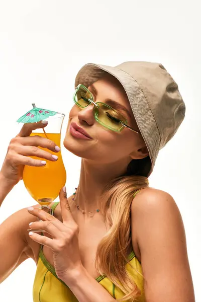 Beautiful young woman sips a colorful drink adorned with a tiny umbrella, radiating joy and style. — Stock Photo