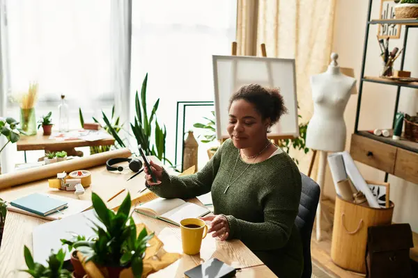 In einer hellen Bastelwerkstatt bastelt eine schöne Frau mit Freude und genießt ein warmes Getränk. — Stock Photo