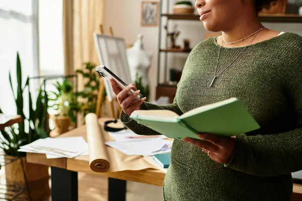 A woman crafts while balancing a notebook and phone, surrounded by creativity. — Stock Photo