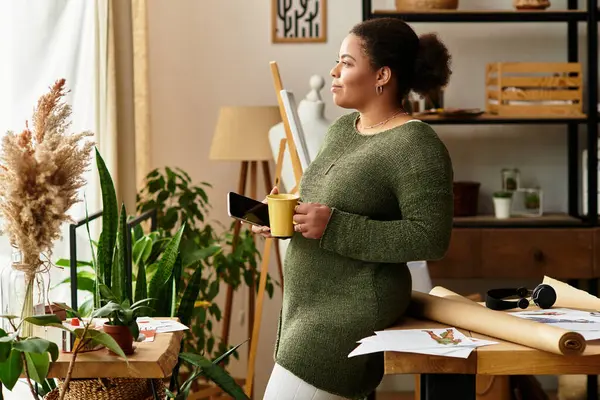 In a cozy workshop, a woman sips a warm drink, thinking of her creative ideas. — Stock Photo