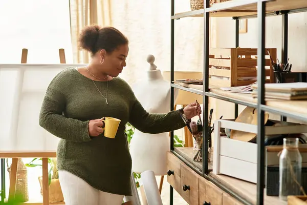 In a cozy crafting workshop, a beautiful woman explores tools while holding a warm drink. — Stock Photo