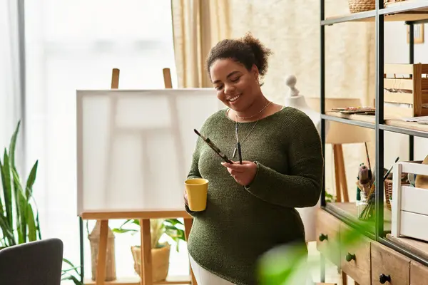 Una bella donna si diverte a lavorare in un laboratorio ben illuminato, sorseggiando un drink e sorridendo. — Foto stock