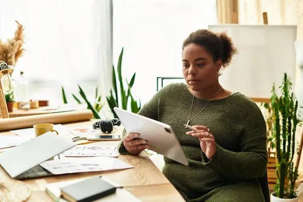 A beautiful woman focuses intently on her design, surrounded by natural light and greenery. — Stock Photo