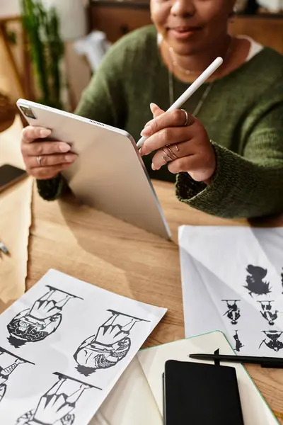 Bella donna si concentra sulla sua opera d'arte digitale mentre circondato da materiali e disegni artigianali. — Foto stock