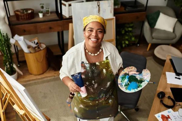 Una mujer talentosa sonríe brillantemente mientras exhibe su paleta de arte llena de colores y pinturas. - foto de stock