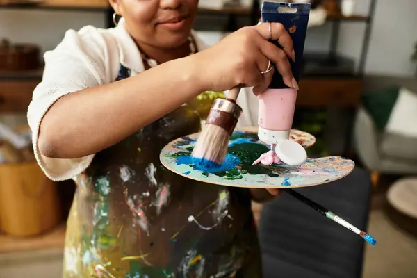 Participando en actividades artísticas, una mujer mezcla alegremente pinturas en un animado taller de artesanía. - foto de stock