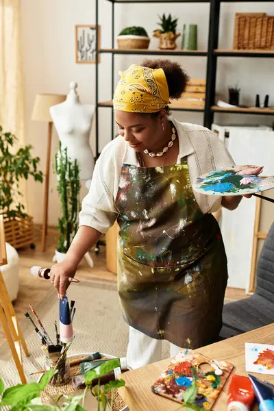 Una hermosa mujer apasionadamente crea arte en un brillante taller rodeado de plantas y materiales - foto de stock