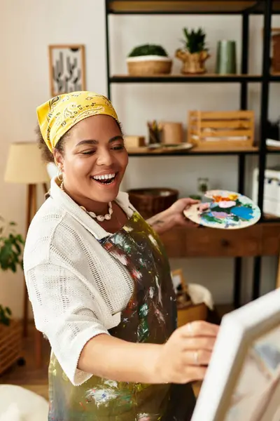Happy woman engaged in painting, surrounded by art supplies in a cozy workshop space. — Stock Photo