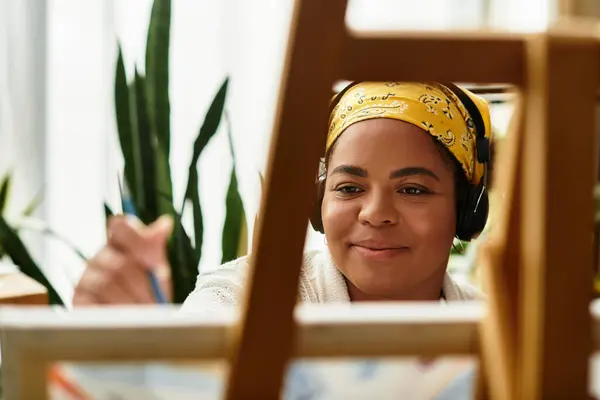 A woman crafts with headphones on, focused on her art in a bright workshop. — Stock Photo