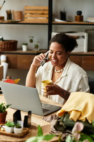 A lovely woman sips tea and chats on her phone at a crafting workshop full of supplies. — Stock Photo