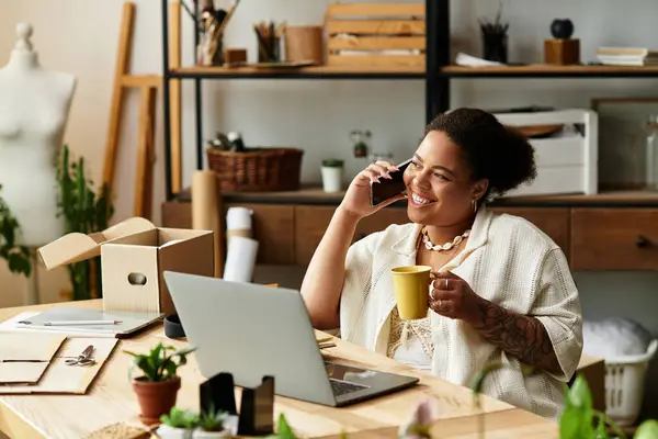 Una hermosa mujer disfruta de su tiempo en un taller de elaboración, hablando por teléfono y bebiendo café. - foto de stock